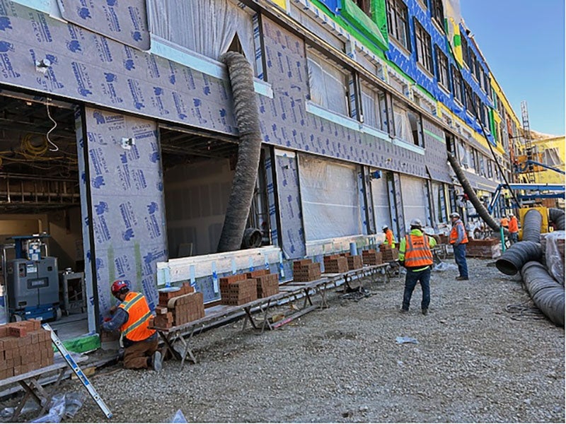 part of a larg building with openings for windows. workers have stacks of bricks next to them as they install them