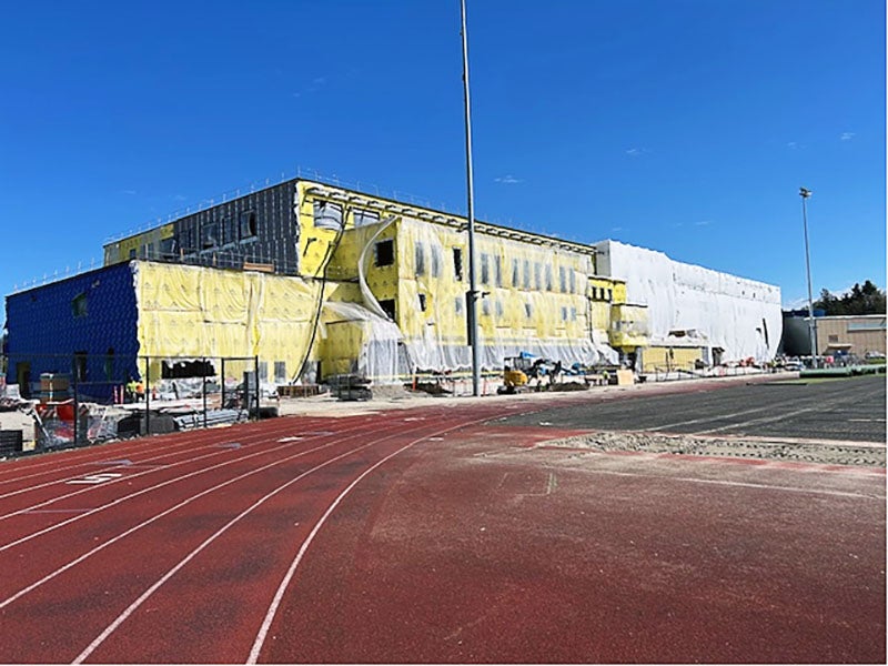 a building under construction has yellow material and plastic on it. a red track is in front.