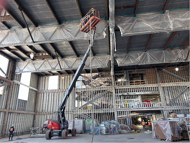 inside a building under construction with metal framing. a lift has a person lifted two the ceiling of the multi-story space