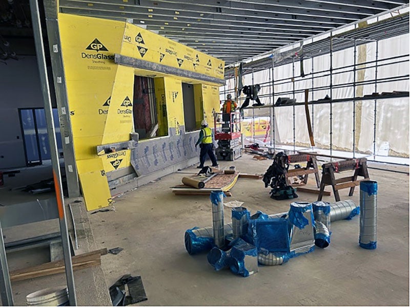 an angled yellow wall with plastic framing with workers on scaffolding
