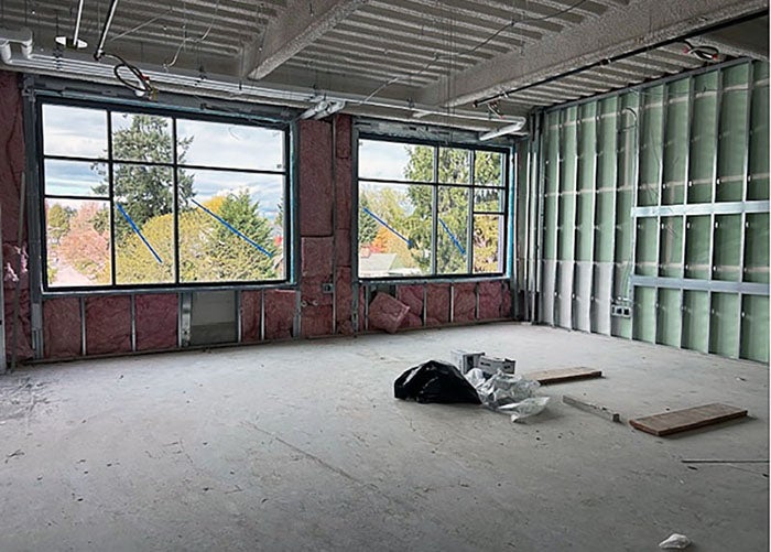 a room with two large windows is under construction with pink insulation around the windows and metal framing on the right wall