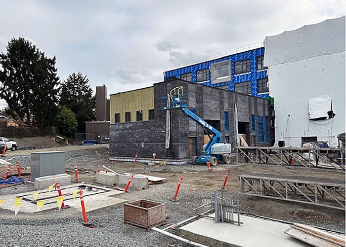 a four story building under construction with metal framing and some yellow wall covering. two lifts and workers are visible