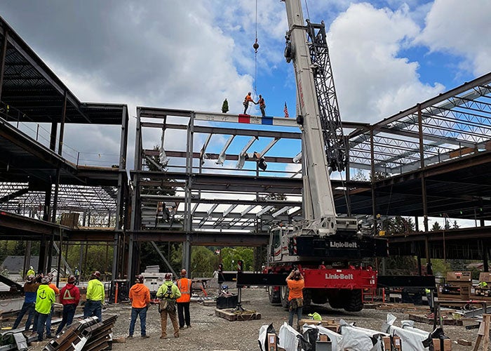 a steel beam frame has two people shaking hands on a white beam with red and blue paint and an evergreen tree and a flag on it