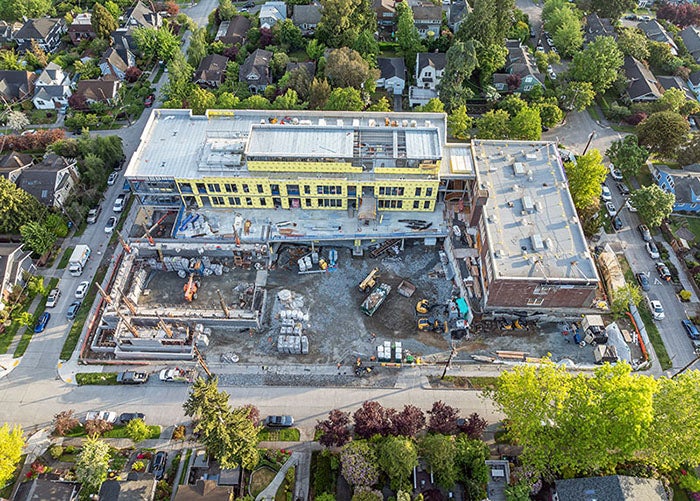 a construction site with a brick building forming an L with a new building. a partially built building is at the other end of the new building