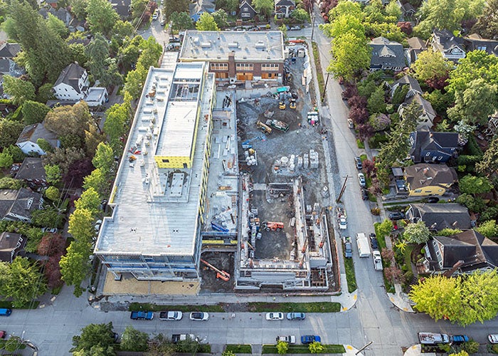 a construction site with a brick building forming an L with a new building. a partially built building is at the other end of the new building