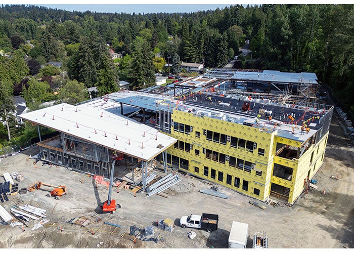a large building under construction with a 3 story section covered in yellow material with writing and a section that has a sloped roof