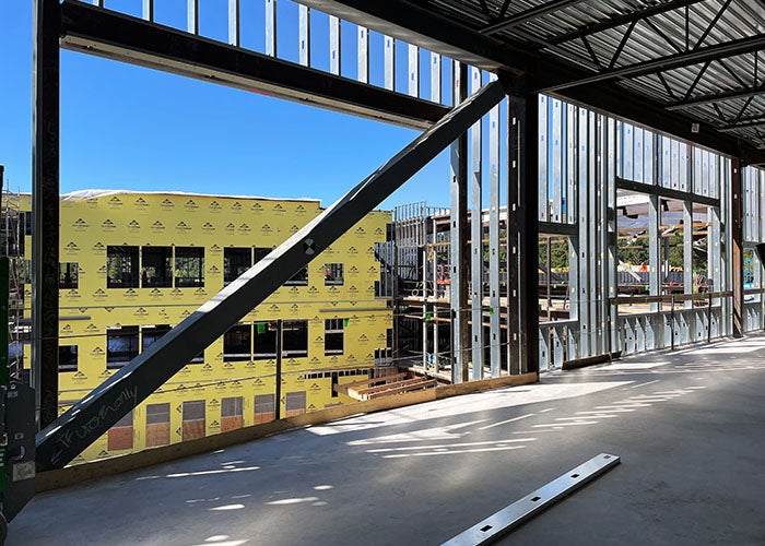 looking out through a wall framing without walls toward another building that has yellow sheathing on it