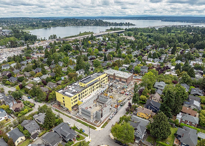 aerial view of entire construction site showing historic brick building, new addition, gym construction in progress, and the surrounding neighborhood with the lake in the background
