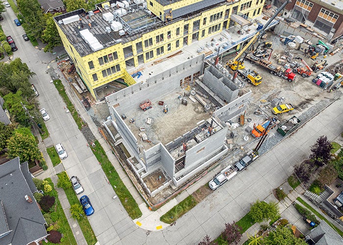 aerial with view of a concrete block building on the corner of the construction site with the new addition above it and part of the historic building to the right