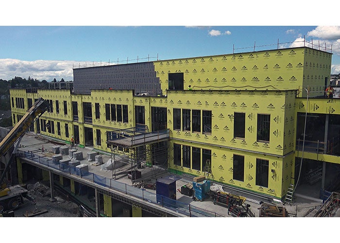 View of the top two stories and the mechanical penthouse of the new addition. below the 2nd floor windows, a large deck area is shown, which currently is holding construction materials