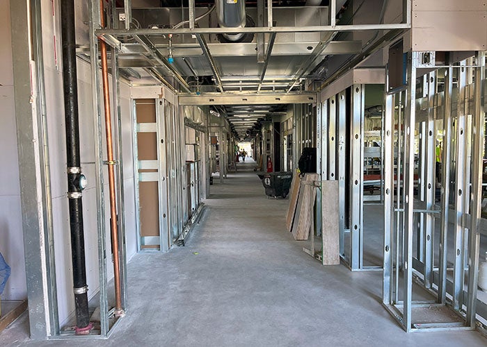 inside a hallway under construction with steel framed walls on each side and utility pipes and conduit showing