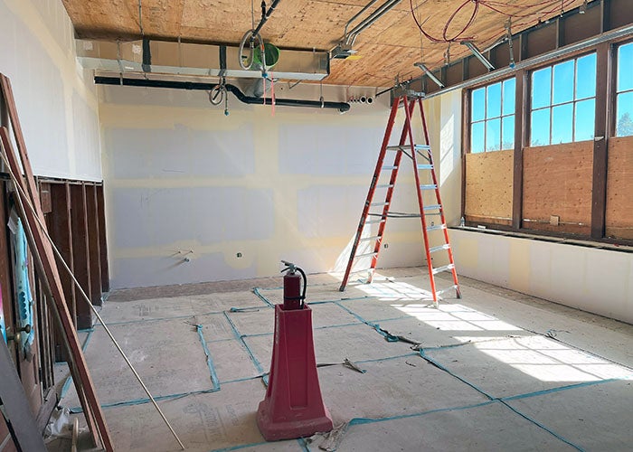 a room under construction with windows on one side and built in cupboards on the other. ductwork and conduit is on the ceiling