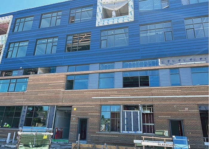 part of a 4-story building under construction with multiple windows. the top two floors have blue metal paneling, there is brick on the other two floors