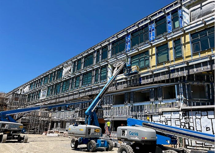 part of a long 4-story building under construction with a lift truck and people working on the windows