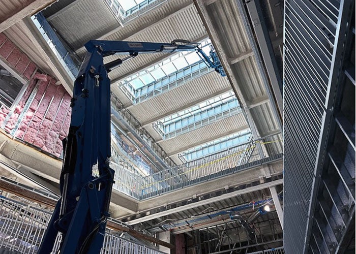 interior of a building under construction looking up toward skylights several floors above. there are metal studs and railings on the side and a lift is raised to the top floor walls