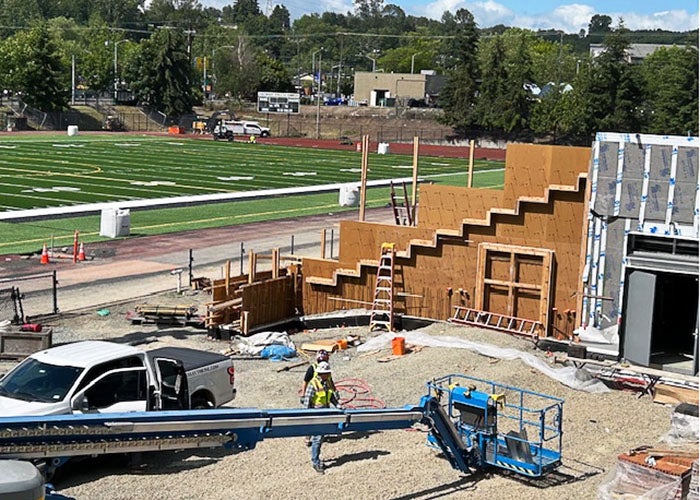 looking toward a green turf field with markings for yard lines a building under construction is in front with a tiered wall
