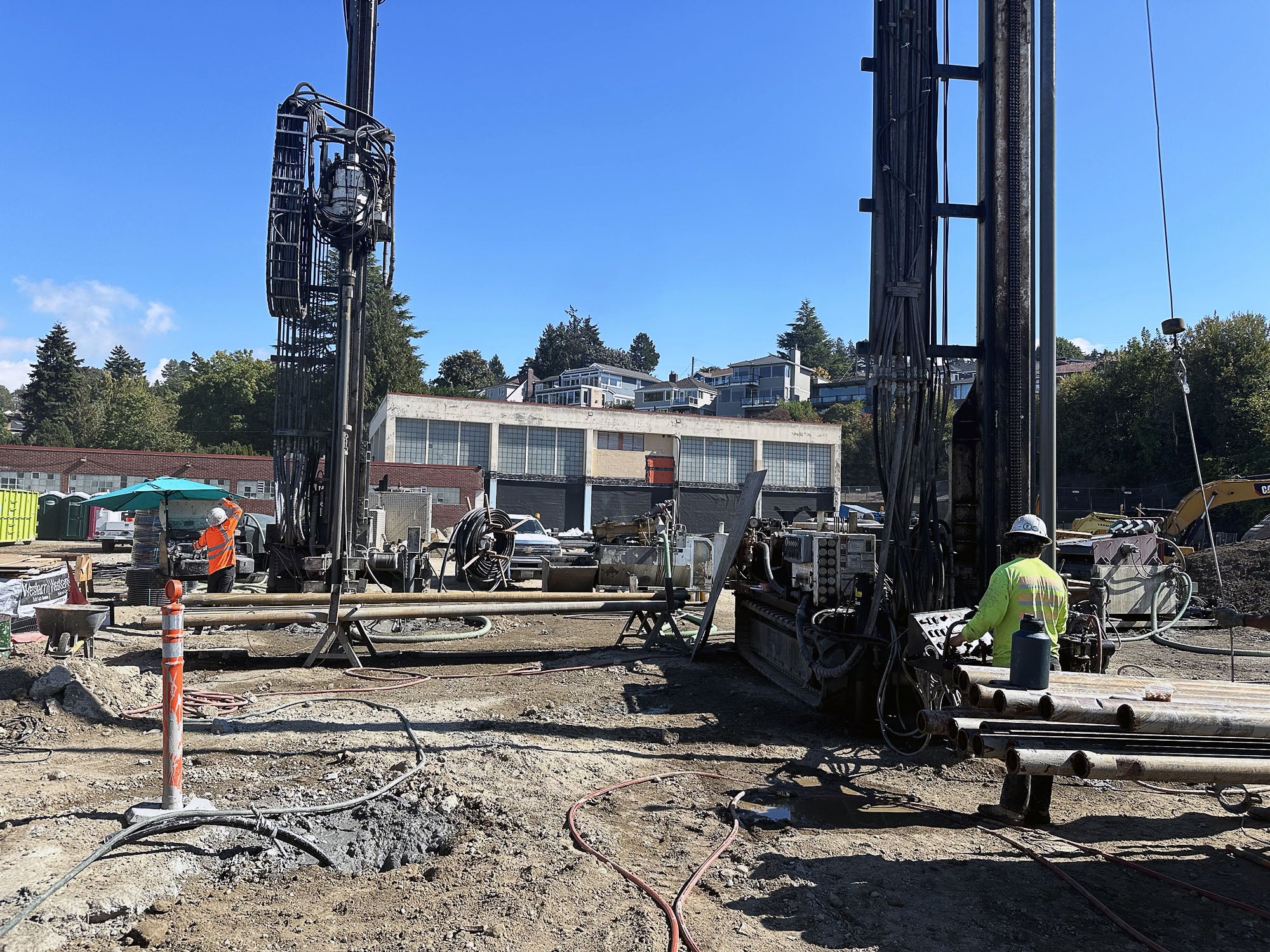 a large drilling rig with a person standing by it in a dirt field with a building behind