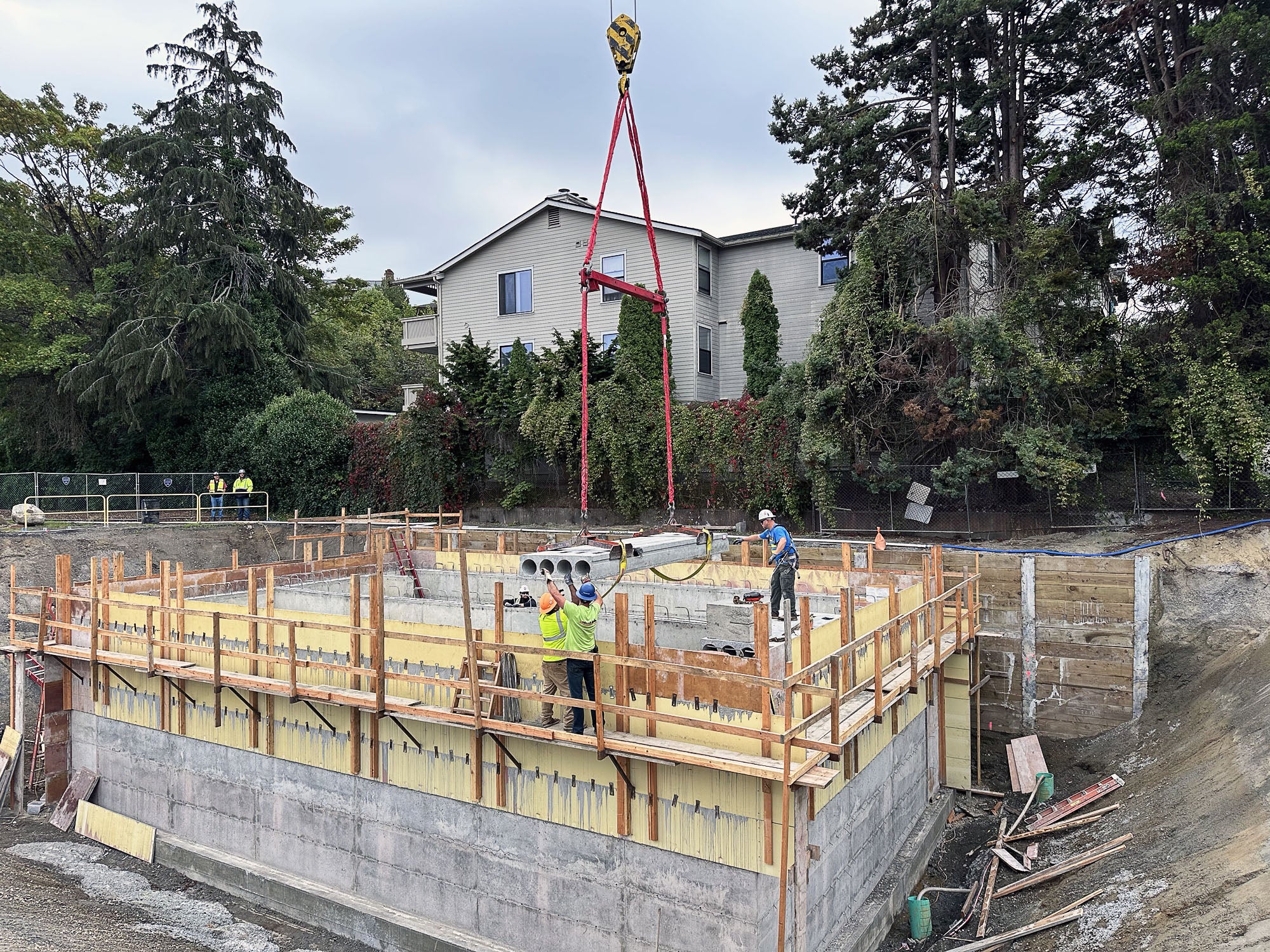 people working to lower material on top of concrete box using a crane