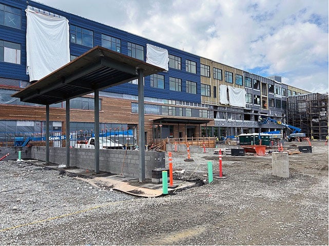 a canopy on steel posts in a gravel yard with a building under construction behind it