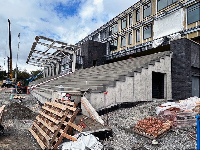 a building under construction with concrete bleachers under construction in front and a frame for a roof over part