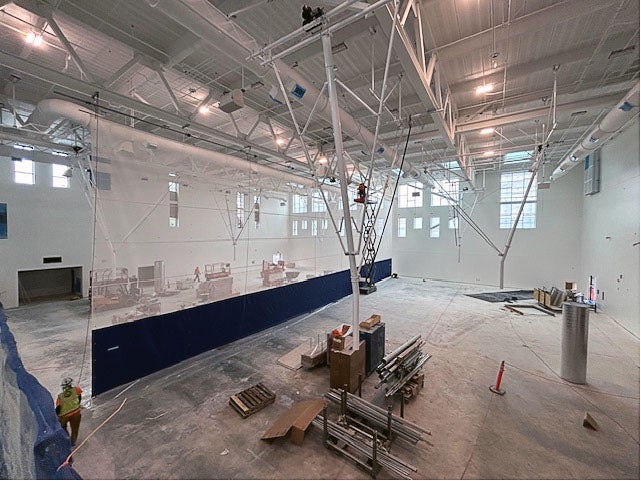 inside a very large room with zig zag rafters and construction equipment and ceiling lights