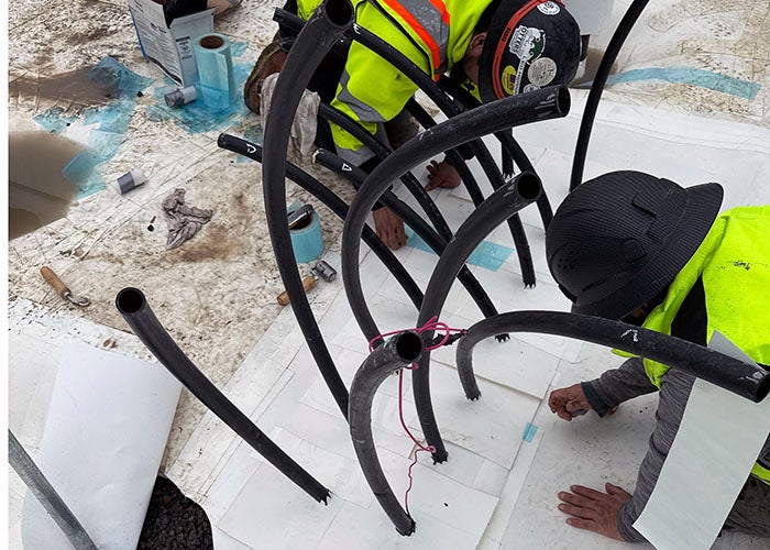 rubber piping sticking up with white material being installed around each pipe by workers