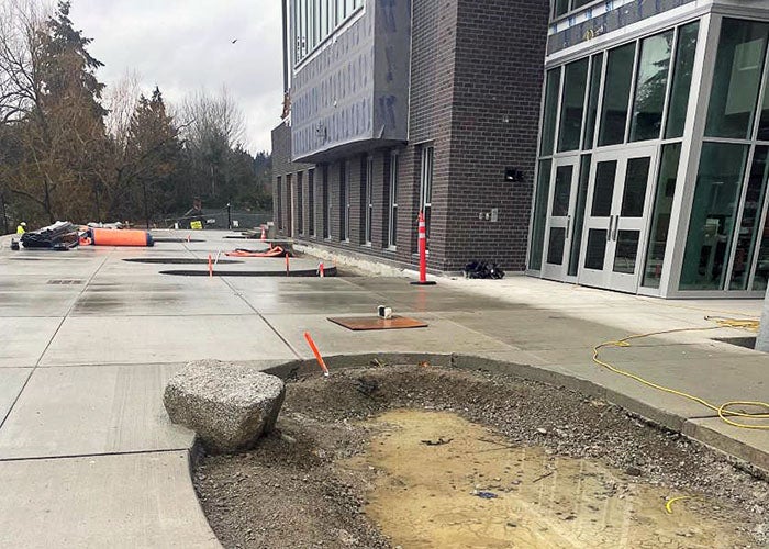 a hole in the middle of a concrete plaza in front of part of a building with doors