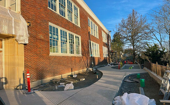 a brick building has a concrete walk way with cutouts for future garden space