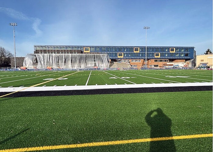 looking across an artificial turf football field toward a building with blue and orange siding