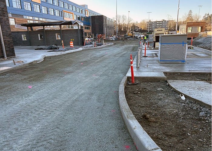 site work with a graded road bed and curb with a building to the left and some construction underway