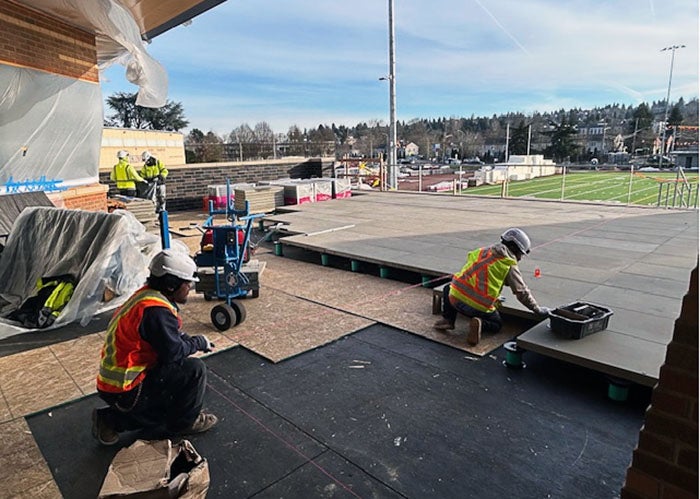 workers are laying pavers on a patio that overlooks a football field