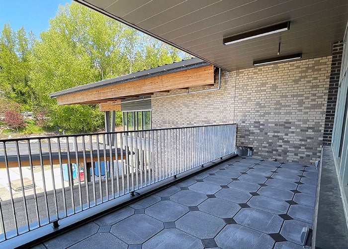 A covered balcony or terrace with modern tile flooring and a metal railing, overlooking other parts of the campus.