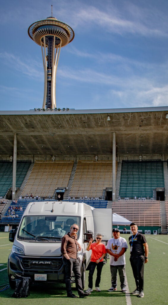 SPSTV crew on the field next to van with Space Needle in the background