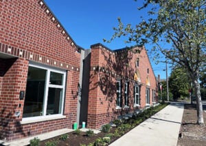 part of a brick building with a sidewalk and deciduous trees
