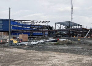 a structural steel frame with a crane in the background and a blue building behind it