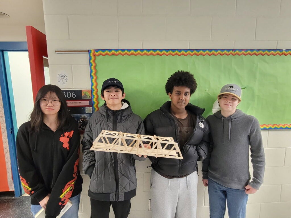 students stand holding popsicle stick bridge