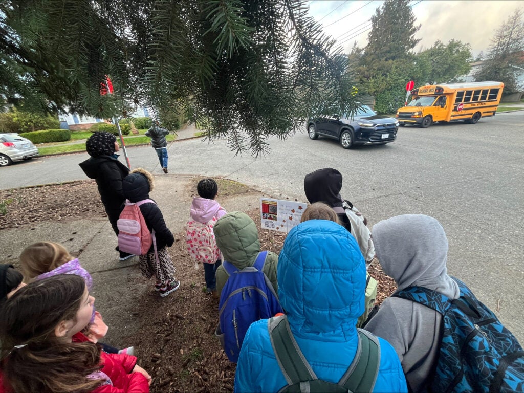 Students gather on the corner of the street by a yard sign featuring a Black artist.