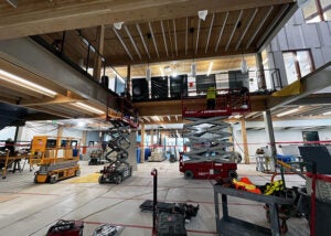 a large space open to the floor above with scissor lifts and people working. the floor is covered in protective cardboard