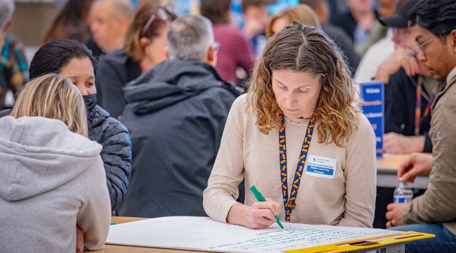 SPS Staff member, Debra Knickerbocker, speaking to community members and writing down key points on a poster board at James Baldwin Elementary School March 26, 2026 community meeting.