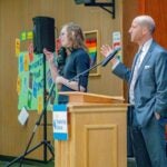Superintendent Shuldiner standing at a podium with a microphone, speaking to community members at Salmon Bay K-8 School March 10, 2026 community meeting.