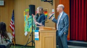 Superintendent Shuldiner standing at a podium with a microphone, speaking to community members at Salmon Bay K-8 School March 10, 2026 community meeting.