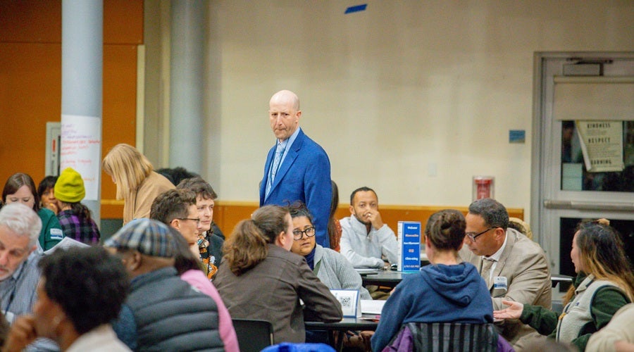 Community members sitting at tables in South Shore Prek-8 School March 3, 2026 community meeting. Superintendent Shuldiner walking around the room, listening to community members.