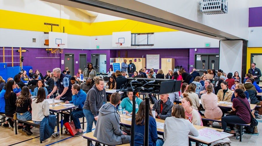 Community members sitting at tables in West Seattle Elementary School gym at March 31, 2026 community meeting