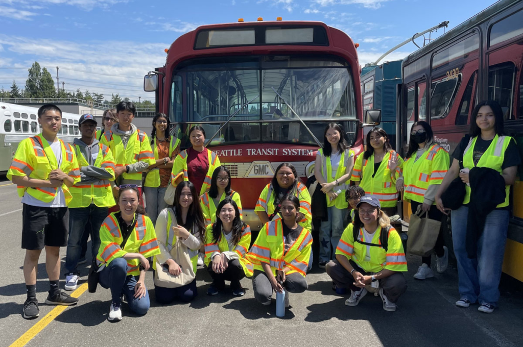 group of students standing in front of a bus wearing yellow safety jackets