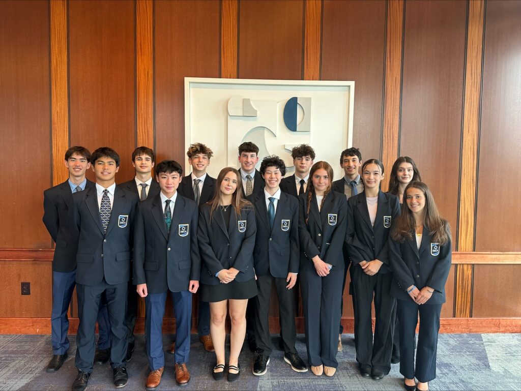 group of students wearing suits and posing in front of a wooden wall with a framed picture in the background