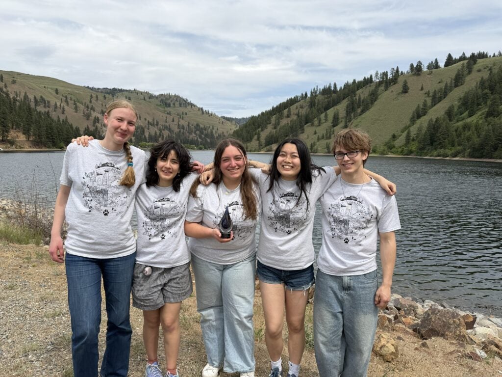 students smiling while wearing matching t-shirts in front of lake with green hills in background