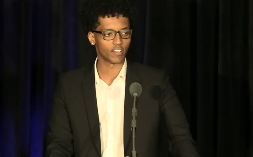student in suit speaking in front of curtains with microphone in foreground