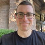 This is a medium close of shot of a smiling man with short hair and glasses.