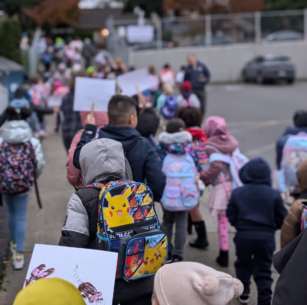 Students walk to school together holding signs.