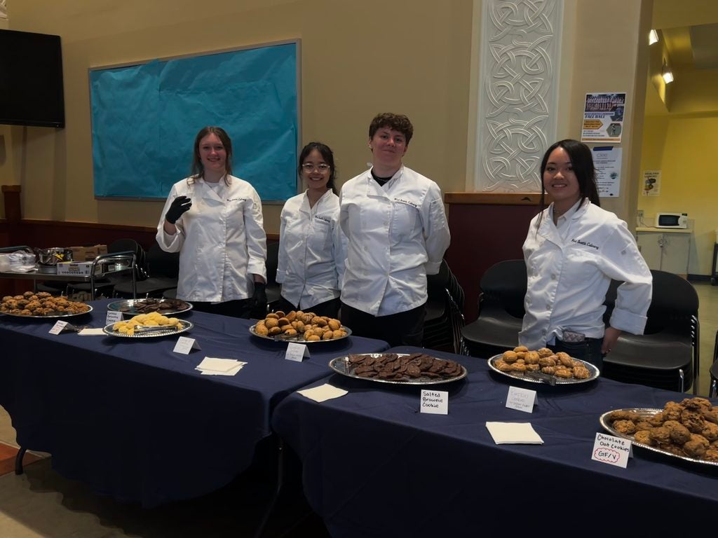 students in chef outfits standing behind dessert table